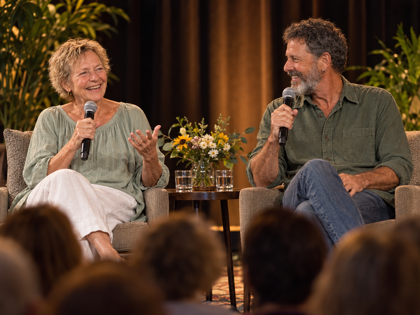 Flip and Rene seated on stage in conversation with microphones, smiling in front of an audience