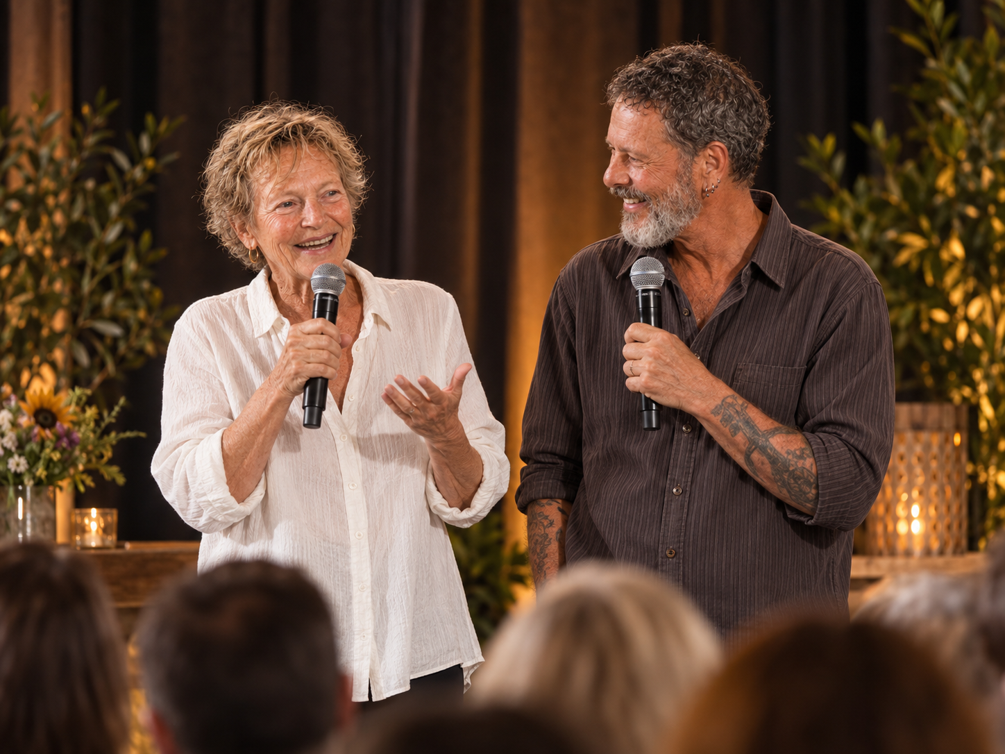 Flip and Rene standing on stage with microphones, warmly engaging an audience